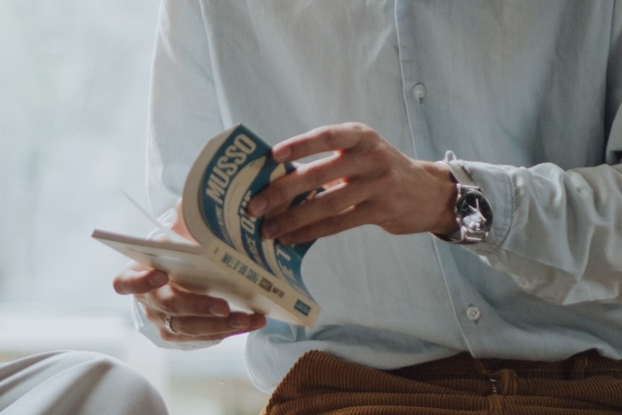 A college student in a button-down wearing a watch reads a book.
