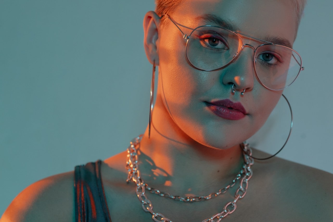 Fashionable lady with glasses wearing a chain necklace stack and large hoop earrings.