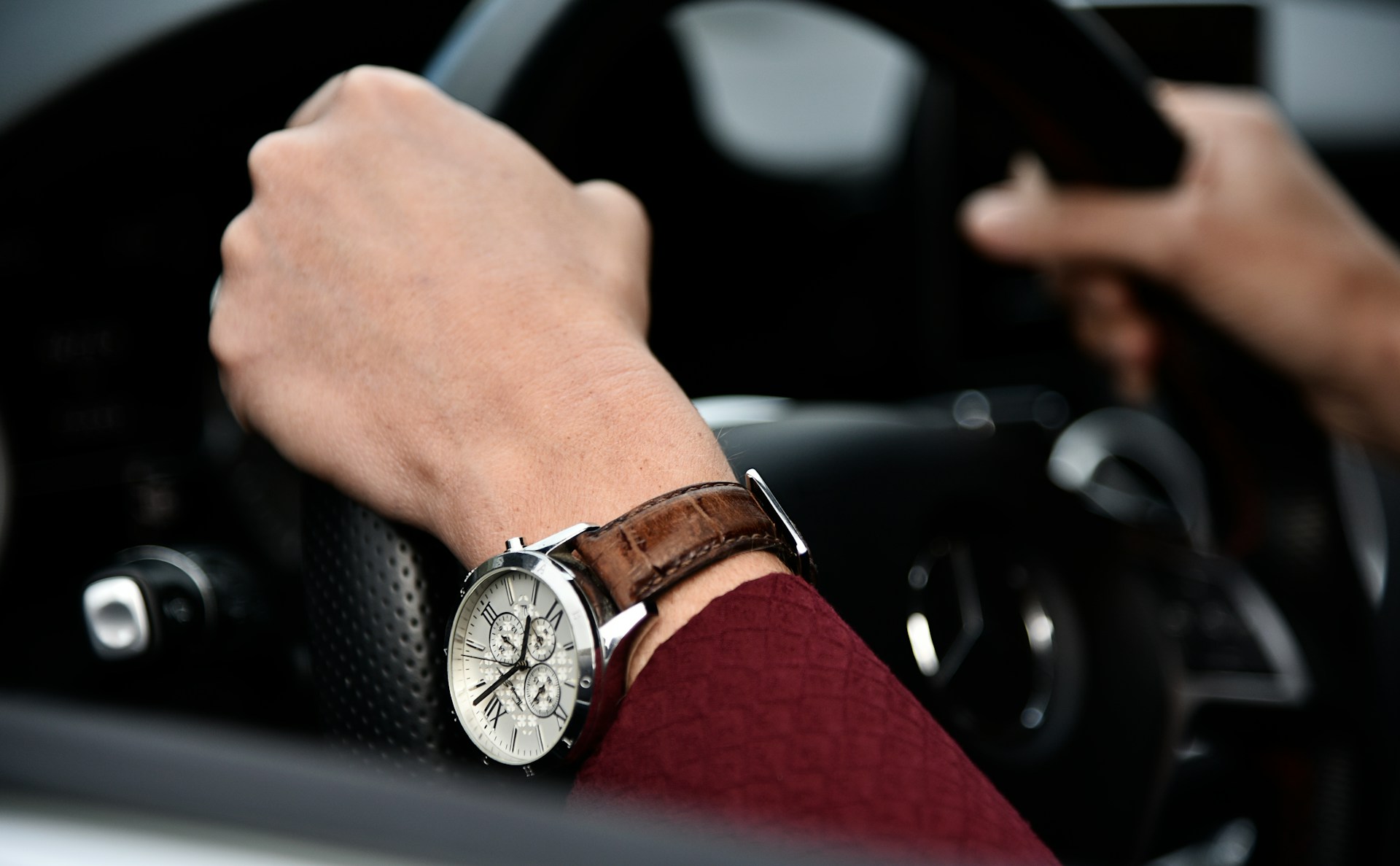 a person’s hands holding a steering wheel and adorned with a luxury watch