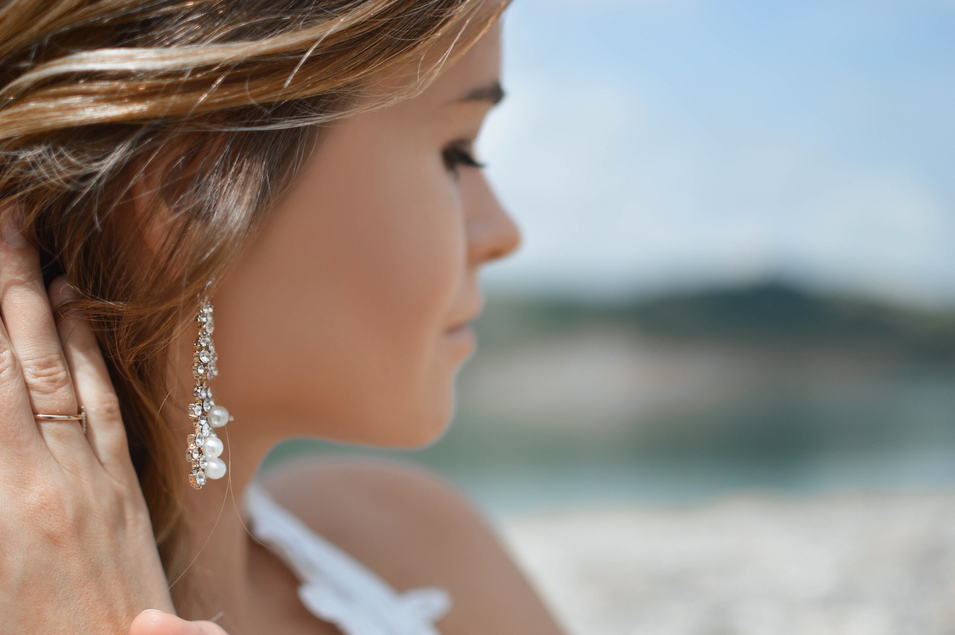 a woman on the beach looking away from the camera and wearing drop pearl earrings