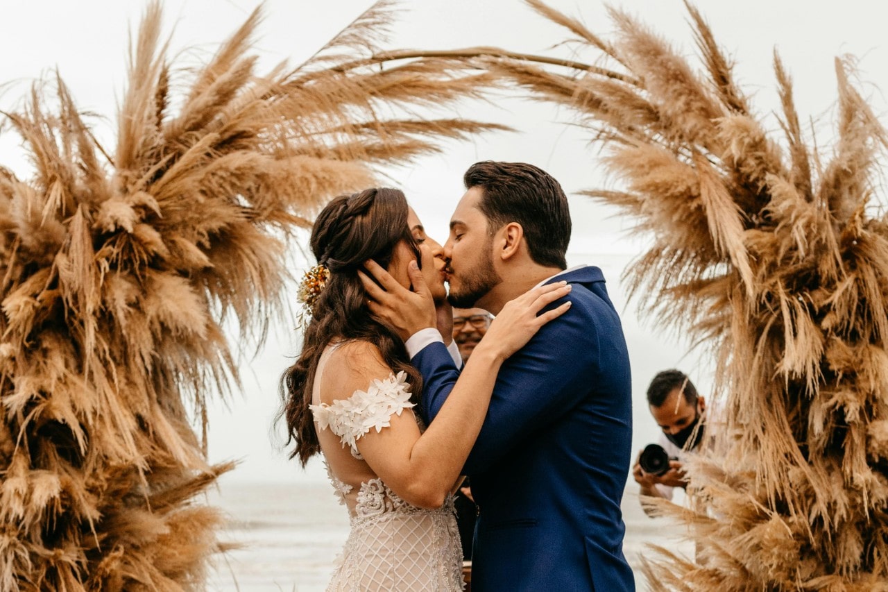 A couple getting married under a brown beach grass arch in the fall.