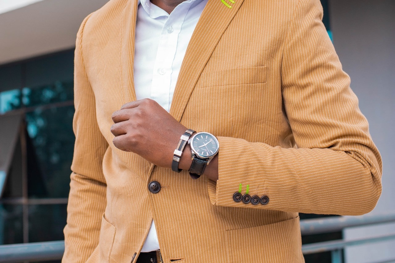 A close-up of a well-dressed man wearing a vibrant blazer, a cuff bracelet, and a luxury watch.