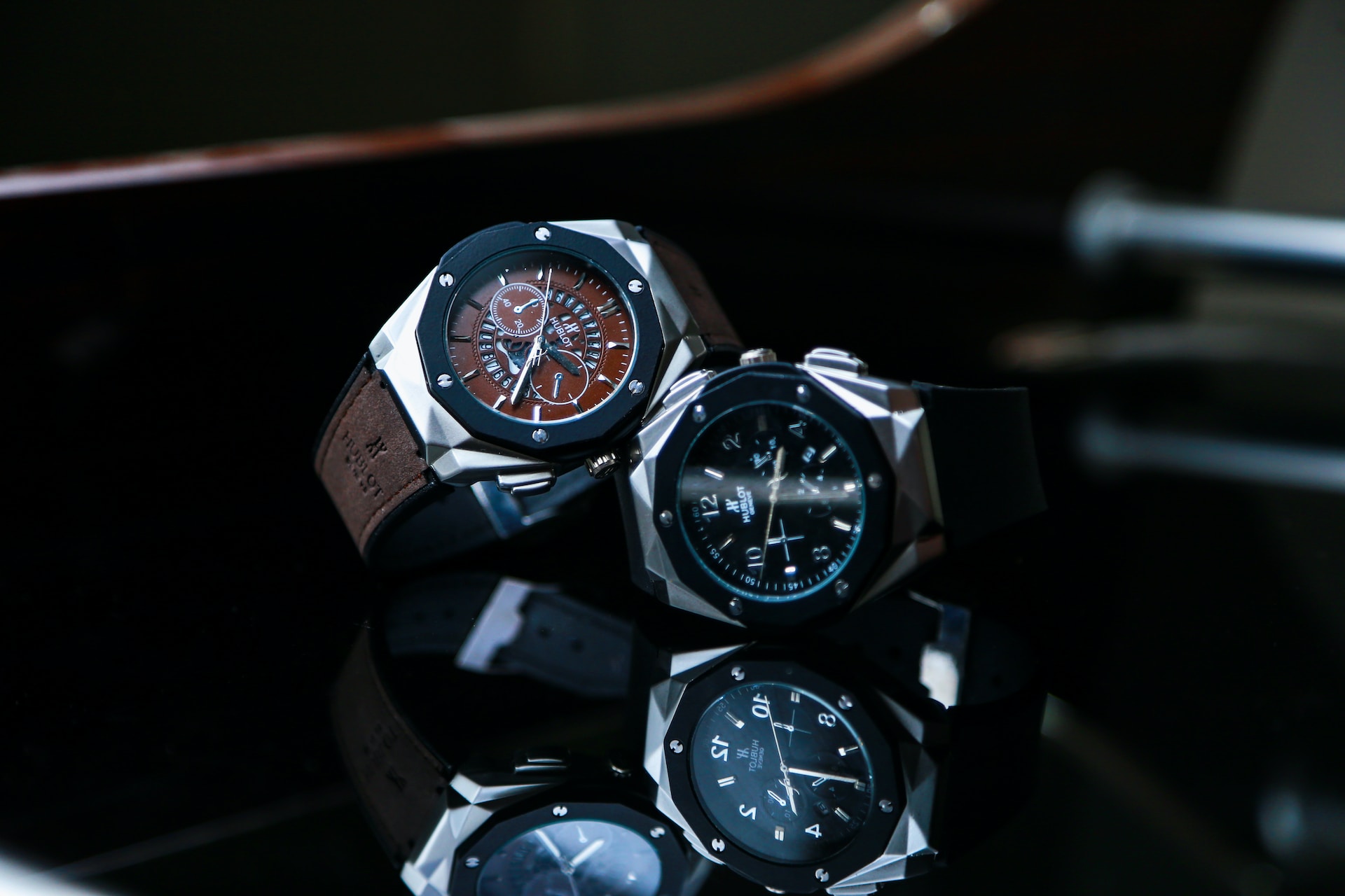 A close-up of two Hublot automatic watches displayed on a reflective glass tabletop.