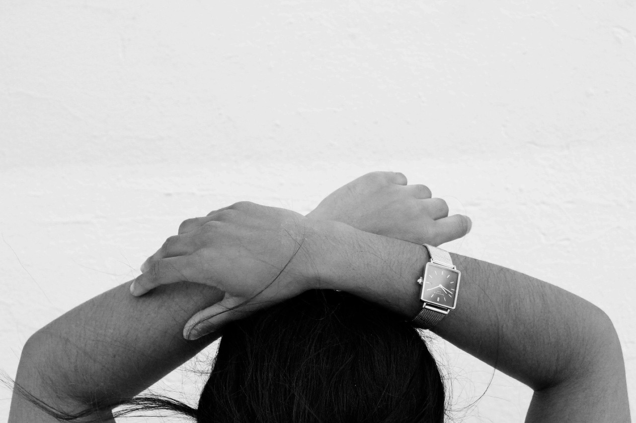 A close-up of a person’s hands, wearing a watch with a square case, resting atop their head.