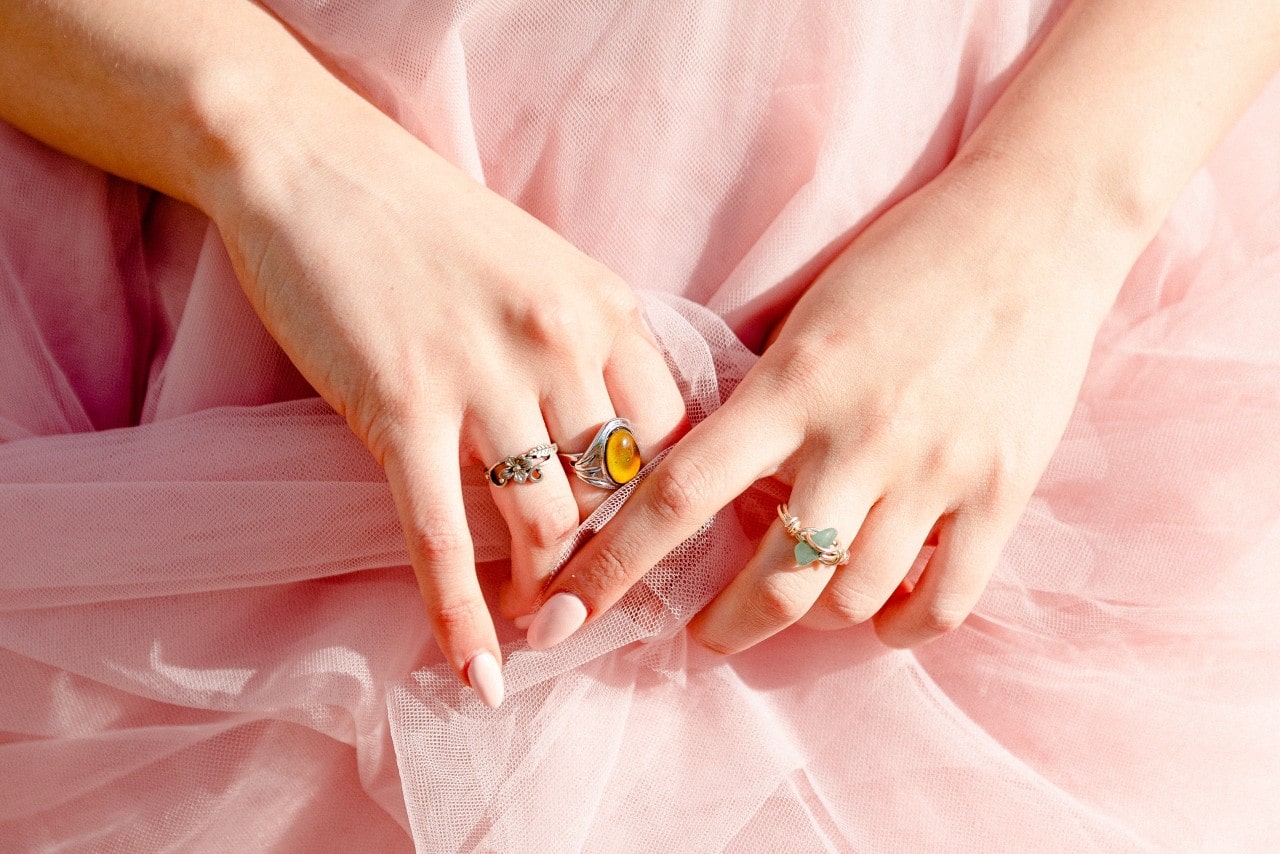 A woman’s hands adorned with pink nails and multiple fashion rings and wearing a pink tulle dress.