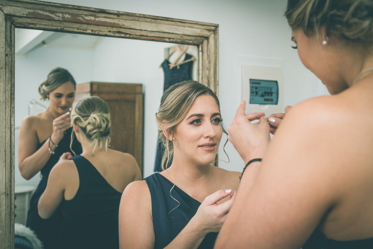 Bridesmaids putting on jewelry in front of a mirror on the wedding day.