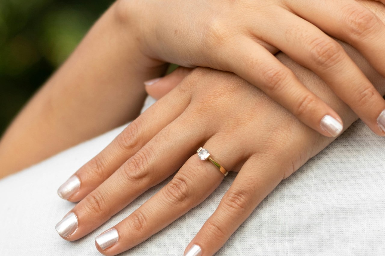 a woman’s hands with silver nails wearing a solitaire engagement ring