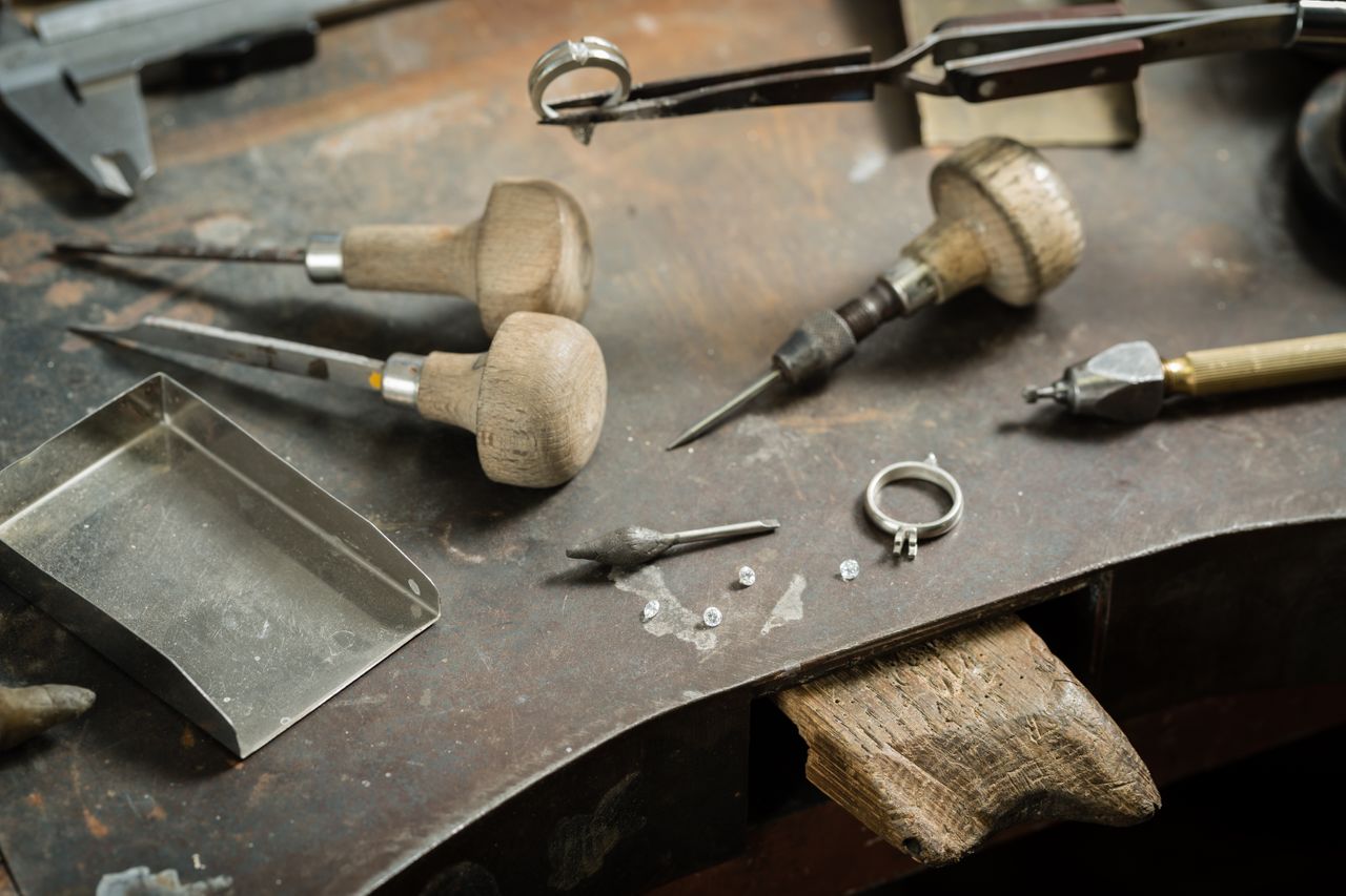 a work desk covered in jewelry-making tools, loose diamonds, and a ring mount