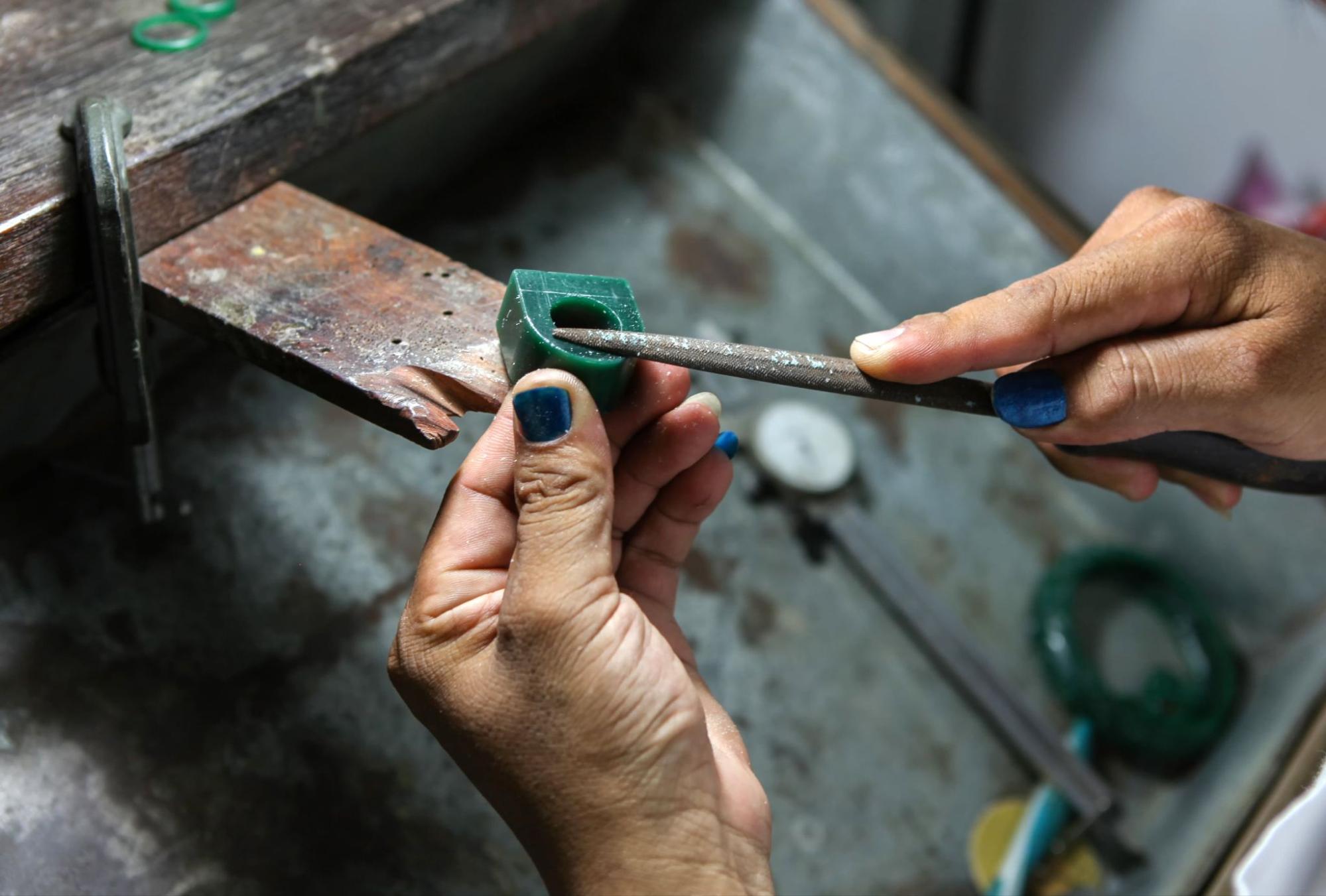 A close-up of a jeweler’s hands carving into a green ring block, creating a custom ring.