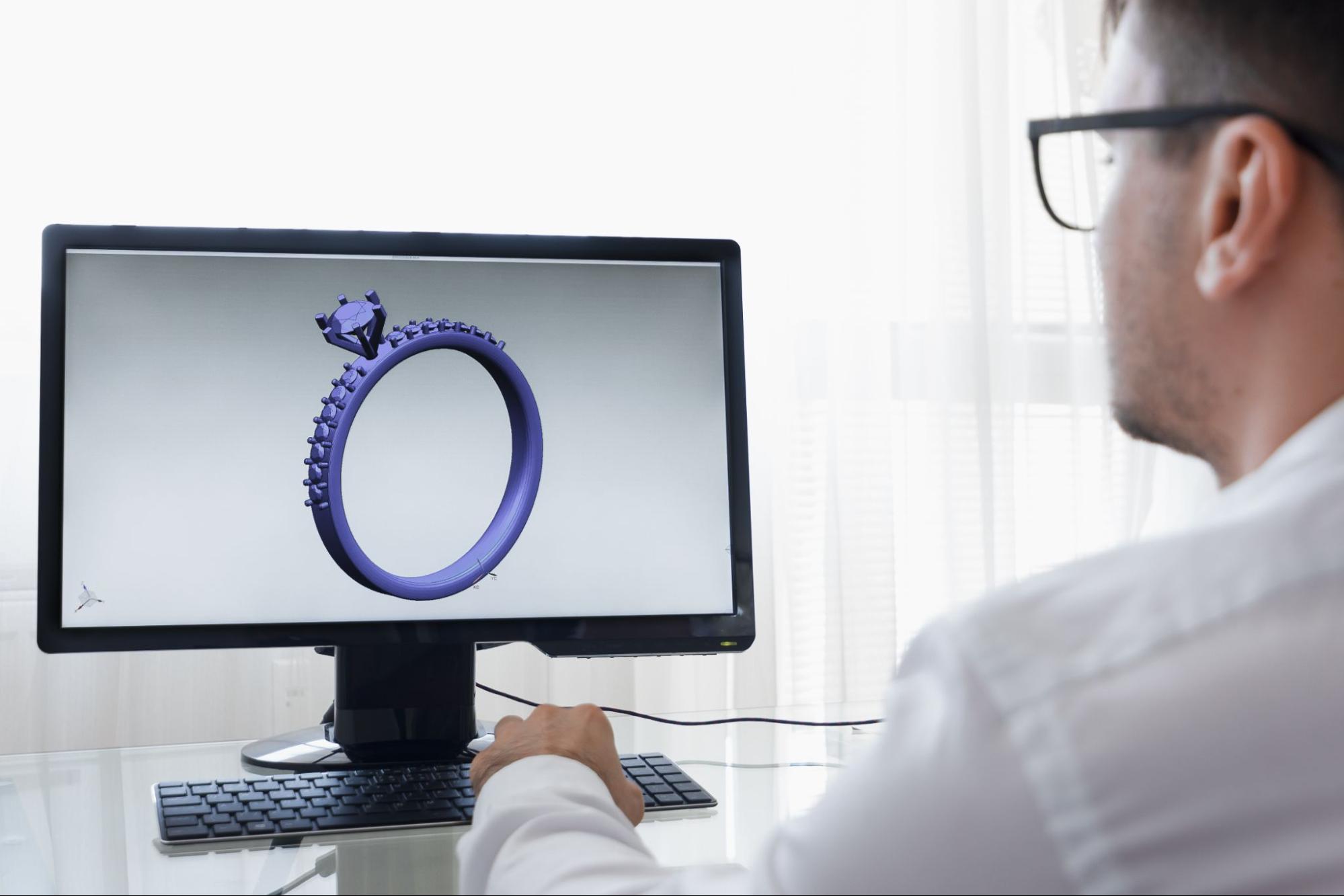 A jeweler looking at a digital rendering of an engagement ring on a computer screen.