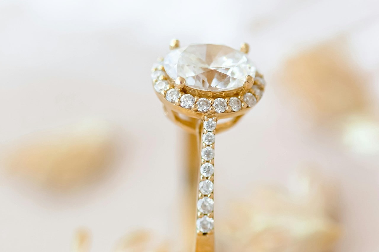 A close-up of a halo gold oval cut halo and side stone engagement ring.