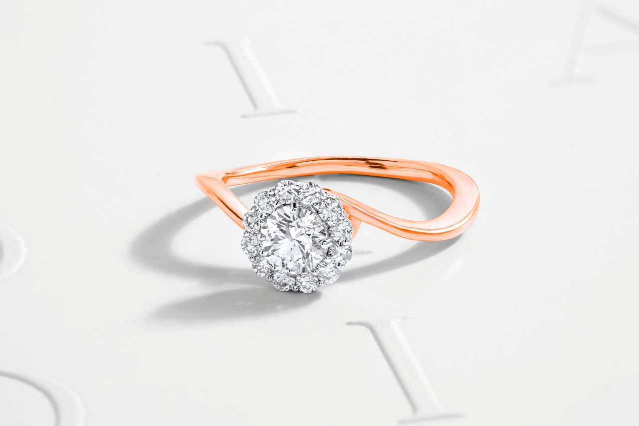 A mixed metal engagement ring with a curvy rose gold band and halo set stone.