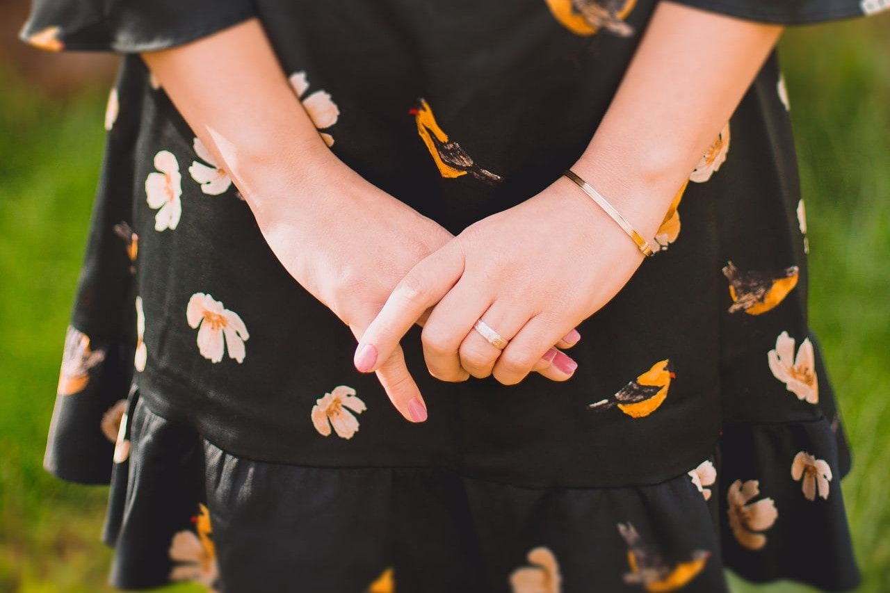 A close-up of a woman wearing a simple gold bracelet and matching ring.