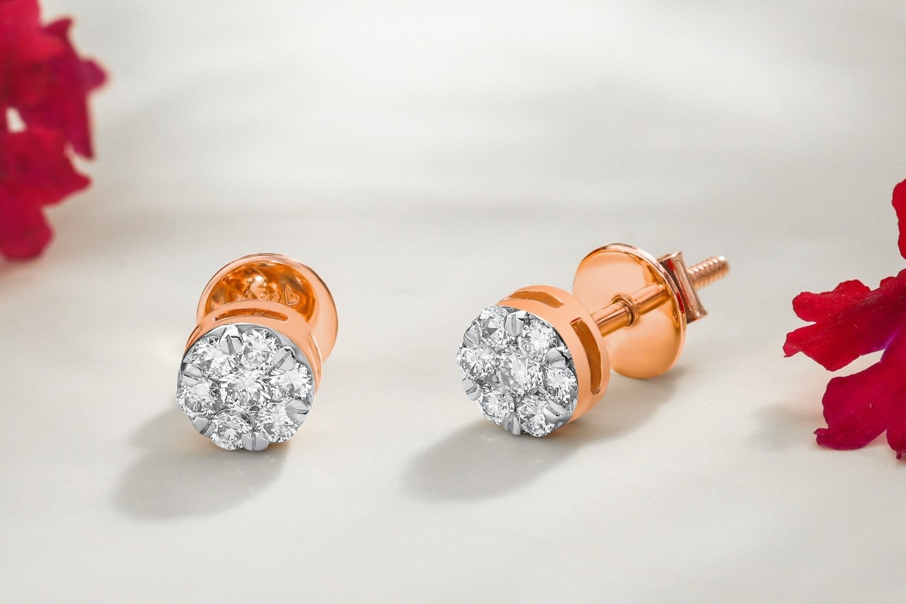 a pair of rose gold diamond stud earrings on a white surface with red flowers.