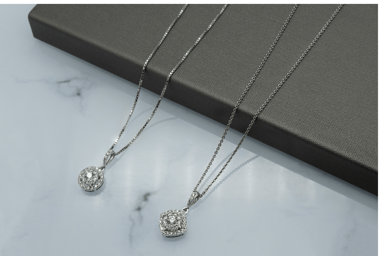 two white gold diamond pendant necklaces on a marble surface.