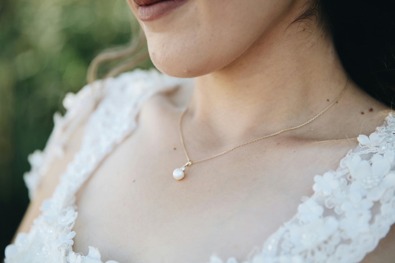 A close-up image of a woman’s neckline adorned with a pearl pendant necklace.