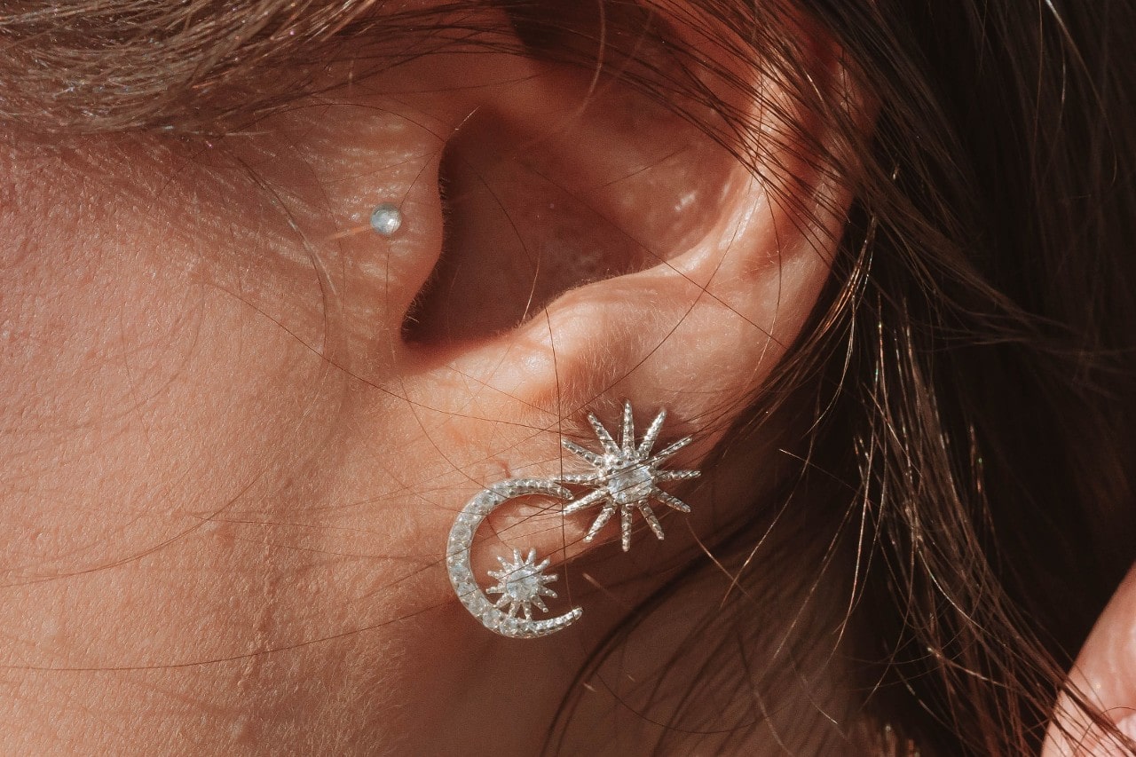 A close-up image of a woman’s heart adorned with three diamond stud earrings.