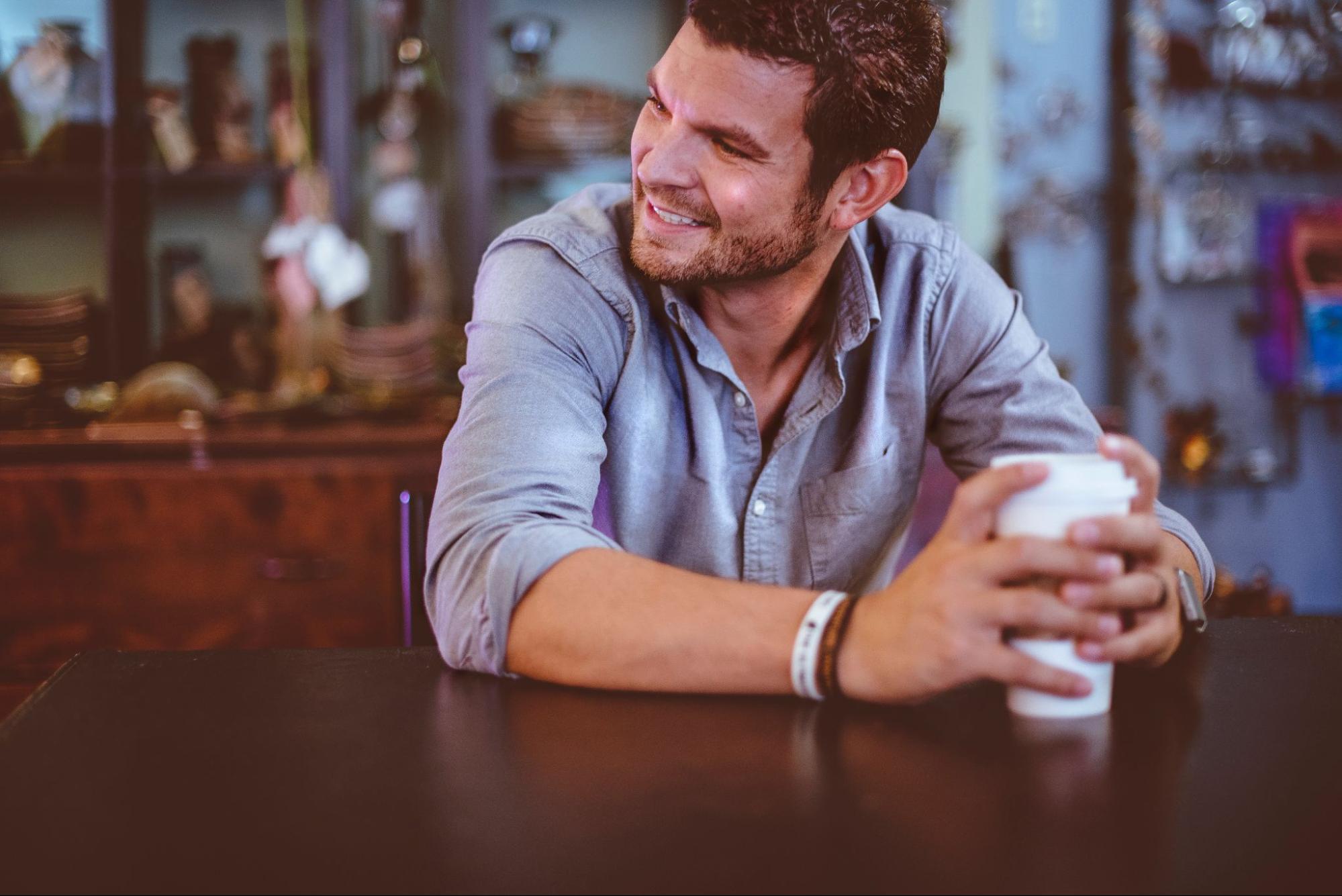 A close-up of a man drinking coffee, wearing fashionable bracelets.