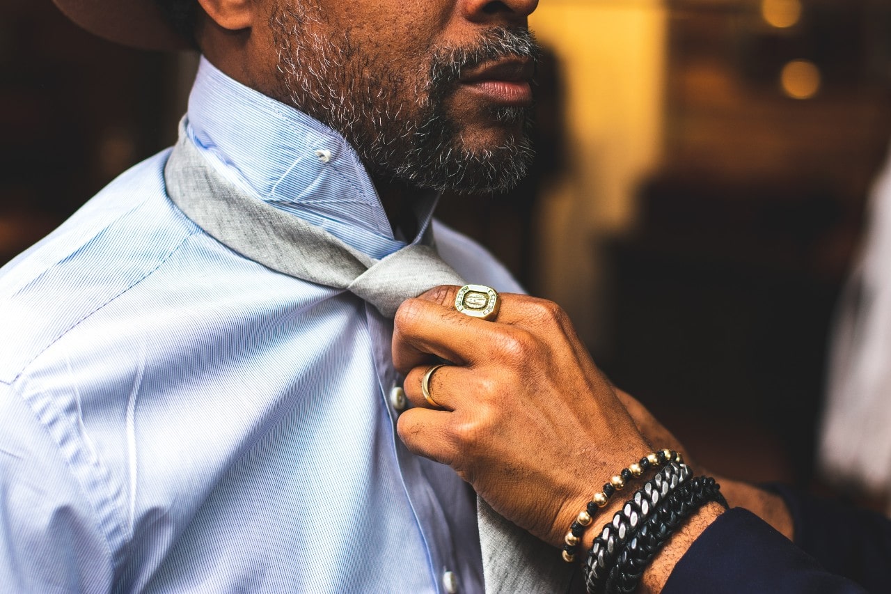 A close-up of a man being dressed by another man wearing a fashionable ring and multiple bracelets.